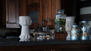 A kitchen with wooden cabinets, a marble countertop, a white decorative vase, and two wooden stools. - Q-Zen House Cunda (Ayvalik)