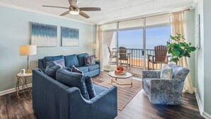 A living room with a sofa, coffee table, and a chair. There is a ceiling fan, a lamp, and artwork on the wall. - Includes Xplorie Activities & Linens. PYRAMID-2BR OFcondo w/outdoor pool. (Ocean City)