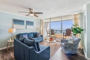 Uma sala de estar com um sofá azul, uma mesa de centro e uma varanda com mobiliário de exterior.
