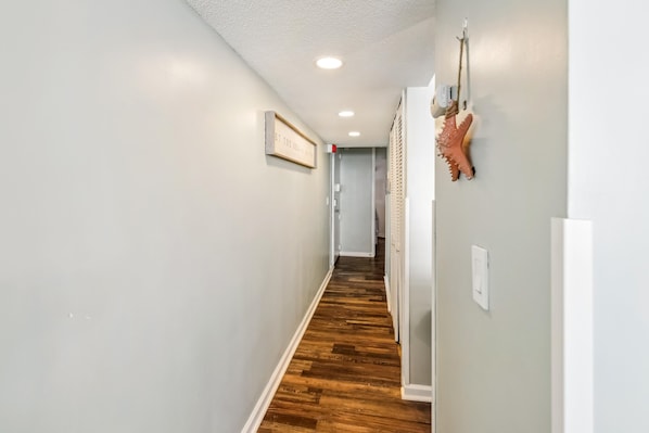 Un couloir avec un plancher en bois, un panneau encadré accroché au mur et une porte au fond.