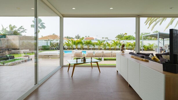 A modern kitchen with a large window, a dining area, and a view of a pool and garden. - Villa Luz de Maspalomas (Maspalomas)