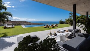 A modern outdoor patio with lounge chairs, a pool, and a view of the ocean.