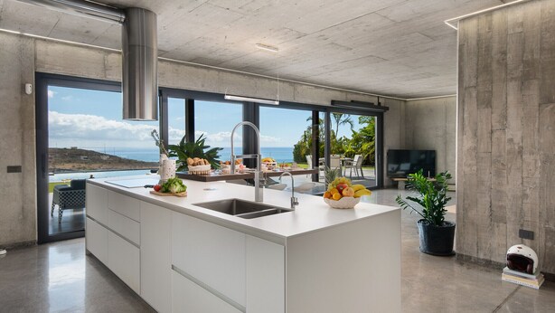 A modern kitchen with a large island, a sink, and a view of the ocean.