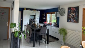 A modern kitchen with white cabinets, a dining area with a table and chairs, and a large window providing a view of the outdoors.