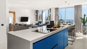 Een moderne keuken met een centraal eiland, blauwe kastjes en een groot raam met uitzicht op de oceaan.