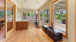 A spacious room with a wooden floor, large windows, and exercise equipment. - Otter Run - Riverfront Paradise in Tumalo, Hot Tub, Sauna, Deck, Pet Friendly! (Tumalo)