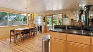 A kitchen with wooden cabinets, a stainless steel trash can, and a dining area with a table and chairs. - Otter Run - Riverfront Paradise in Tumalo, Hot Tub, Sauna, Deck, Pet Friendly! (Tumalo)