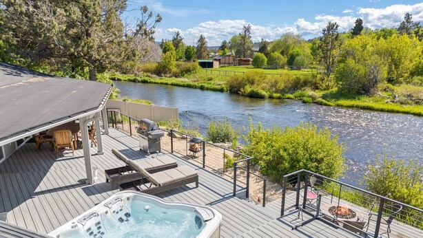 A deck with a hot tub, lounge chairs, and a fire pit overlooking a river. - Otter Run - Riverfront Paradise in Tumalo, Hot Tub, Sauna, Deck, Pet Friendly! (Tumalo)