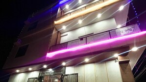 Un edificio con un letrero que indica servicio las 24 horas, una motocicleta estacionada frente a él, y una escalera que lleva a la entrada.