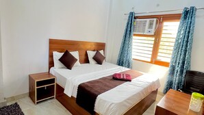 Un dormitorio con cama, mesitas de noche, aire acondicionado y ventana con cortinas.