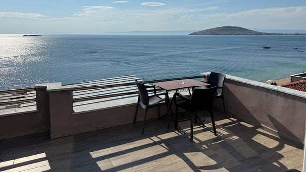 Un balcon avec une table et des chaises, donnant sur une étendue d’eau où l’on peut voir des bateaux et, au loin, une île.