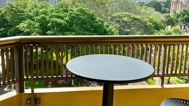 A balcony with a round table and two chairs, overlooking a cityscape with tall buildings and lush greenery.