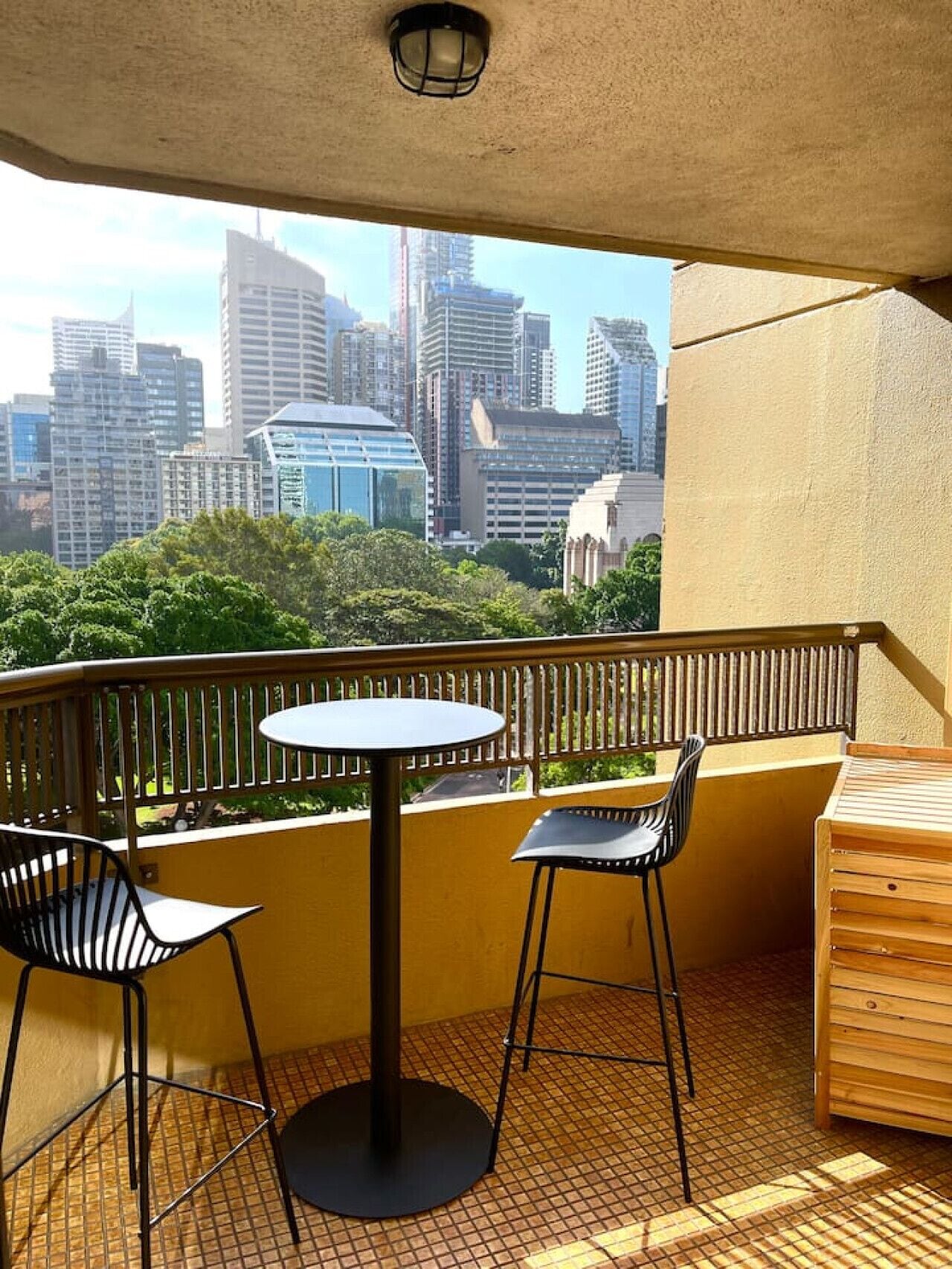 A balcony with a table and chairs, a view of a city skyline, and a wooden bench.