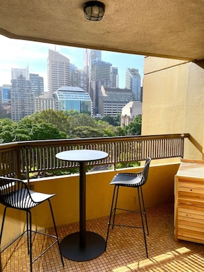 Un balcon avec une table et des chaises, une vue sur les toits de la ville et un banc en bois.