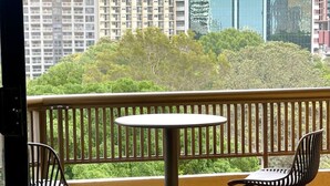Ein Balkon mit rundem Tisch und zwei Stühlen, der auf einen Stadtblick mit Hochhäusern und Grünflächen blickt.
