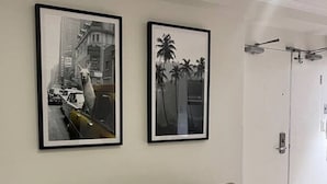 Ein Wohnzimmer mit einem beigefarbenen Sofa, zwei gerahmten Bildern an der Wand, einer Tür und einer braunen Decke auf dem Sofa.