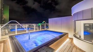 Ein Pool auf dem Dach mit Glasgeländer, einer Whirlwanne und Blick auf die Stadt bei Nacht.