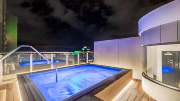 A rooftop pool with a glass balustrade, a hot tub, and a city view at night.