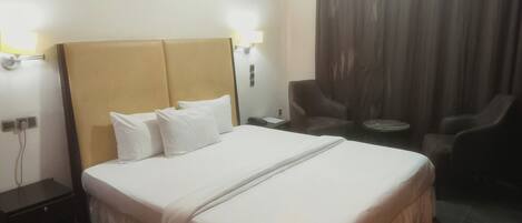A hotel room with a large bed, a nightstand, a chair, and a small table.