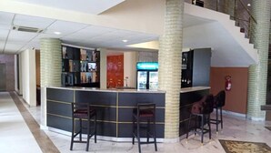 Un hall con mostrador de recepción, dos taburetes de bar, un refrigerador y una escalera.