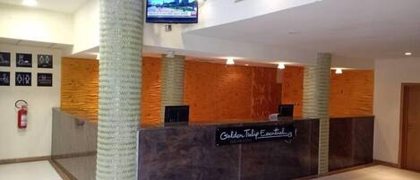 A hotel reception desk with a modern design, featuring a wooden panel wall and a glass column.