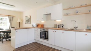 Eine moderne Küche mit weißen Schränken, einer Holz Arbeitsplatte, einem eingebauten Ofen und einem Spülbecken. Über dem Spülbecken befinden sich Regale mit Dekorationen.