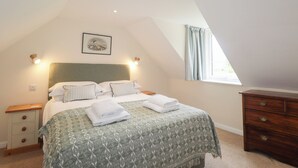 Ein Schlafzimmer mit Bett, Nachttisch, Kommode, einem Fenster mit Vorhängen und einer Deckenleuchte.