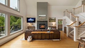 A spacious living room with a large brown leather sofa, a fireplace, a television, and a staircase. - Island Escape with Comfort and Privacy -Margo House (Friday Harbor)