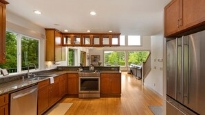 A modern kitchen with wooden cabinets, stainless steel appliances, and large windows offering a view of the outdoors. - Island Escape with Comfort and Privacy -Margo House (Friday Harbor)