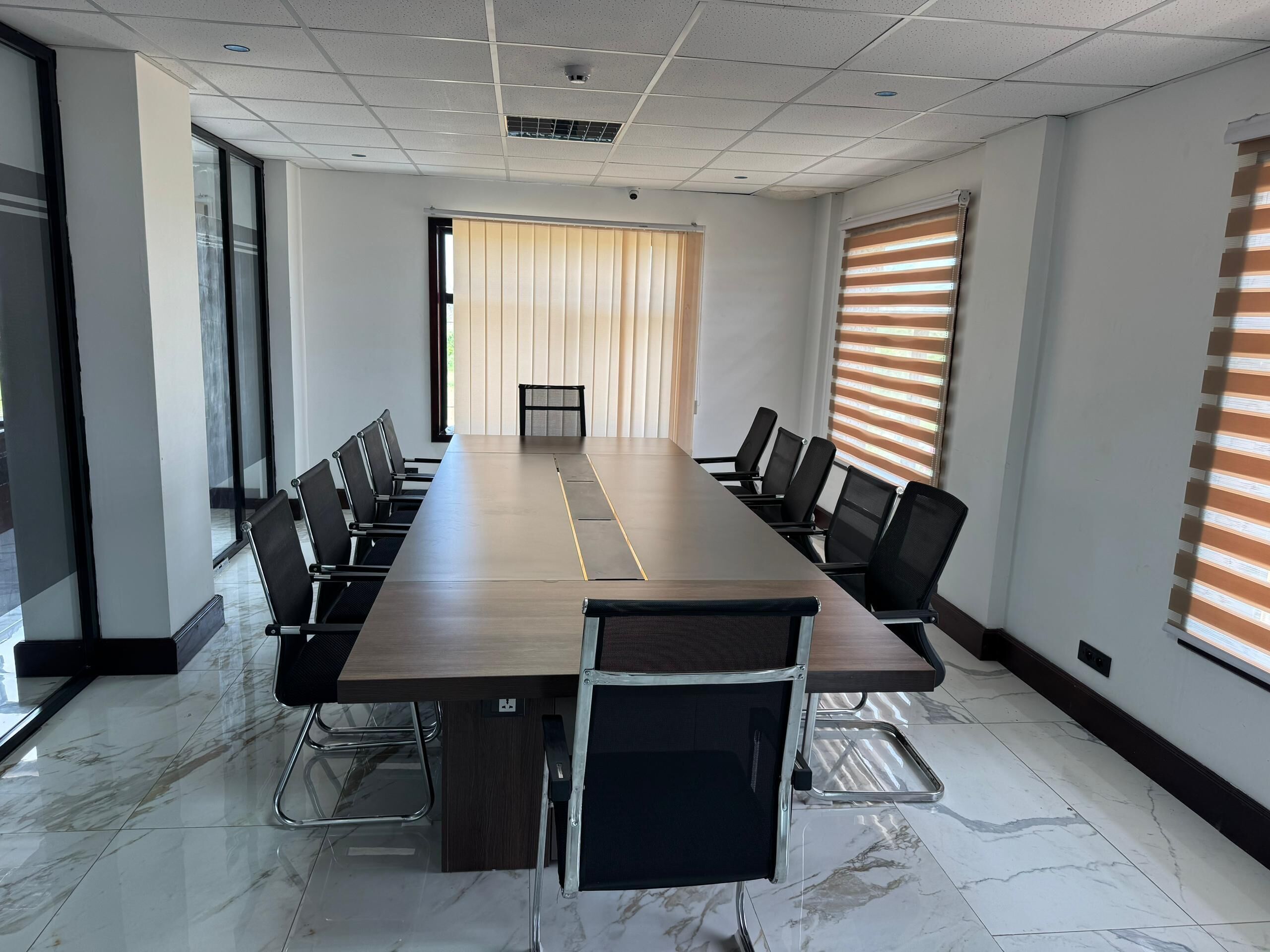 A conference room with a long table, black chairs, and a view of a building through a large window.