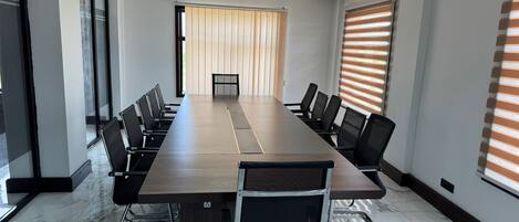 A conference room with a long table, black chairs, and a view of a building through a large window.