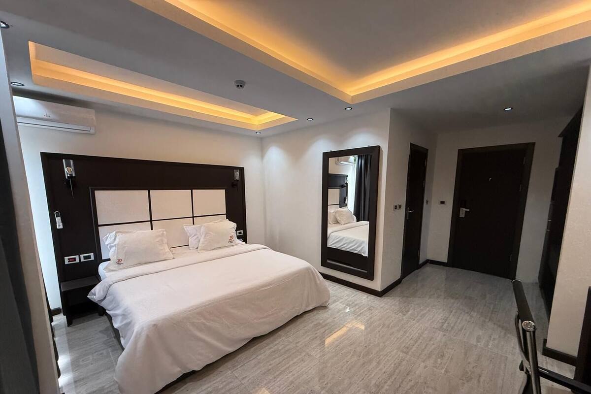 A modern hotel room with a large bed, a built-in mirror, and recessed lighting.