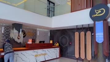 A hotel reception area with a marble counter labeled "RECEPTION," a modern chandelier, and a large logo on the wall.