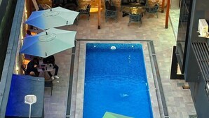 Una piscina al aire libre con un borde de azulejos, rodeada de sillas de descanso y sombrillas.