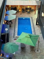 Una piscina al aire libre con un borde de azulejos, rodeada de sillas de descanso y sombrillas.