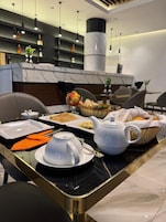Desayuno servido en una mesa de mármol, con una tetera blanca y diversas opciones para el desayuno.