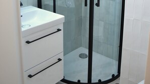 A modern bathroom with a glass-enclosed shower, a white sink with black handles, and a tiled floor.