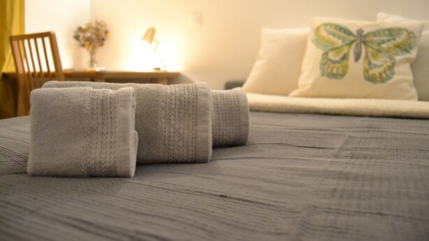 A neatly made bed with folded towels, a lamp on a bedside table, and a butterfly pillow on the headboard.