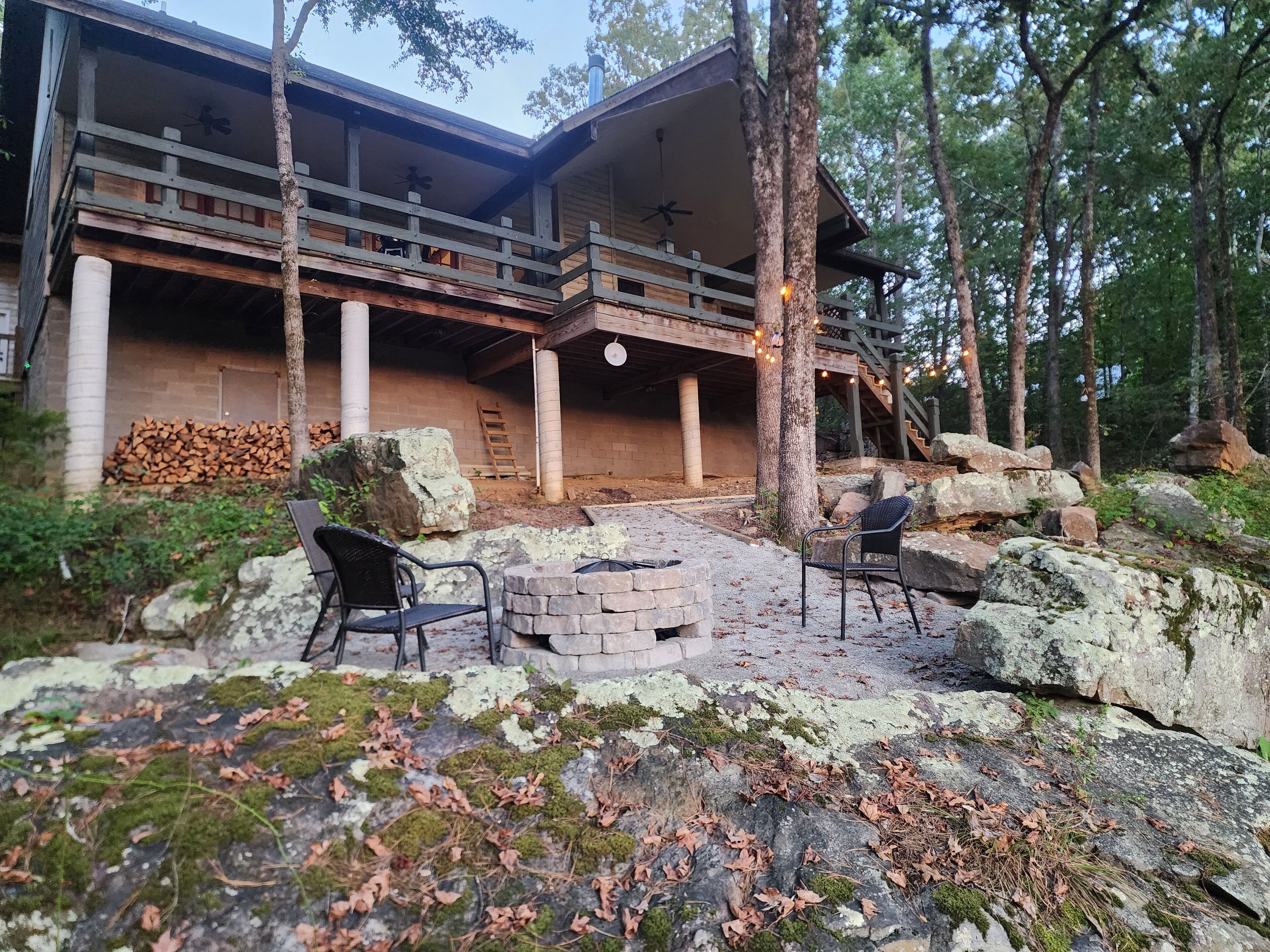 Une cabane en rondins à deux étages, dotée d’un balcon, d’un foyer en pierre et de sièges d’extérieur.