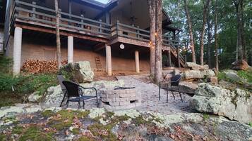 Une cabane en rondins à deux étages, dotée d’un balcon, d’un foyer en pierre et de sièges d’extérieur.