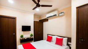 Ein Hotelzimmer mit Bett, Deckenventilator, Klimaanlage, Fernseher und Holztüren.