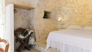 A stone-walled bedroom with a bed, a chair, and a shelf with a bottle.