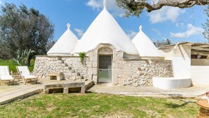 A stone building with a conical roof, a door, and a small porch with chairs.