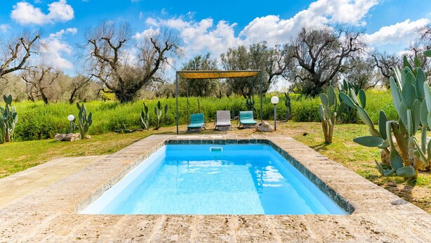 A rectangular swimming pool with a wooden pergola and two lounge chairs in the background.