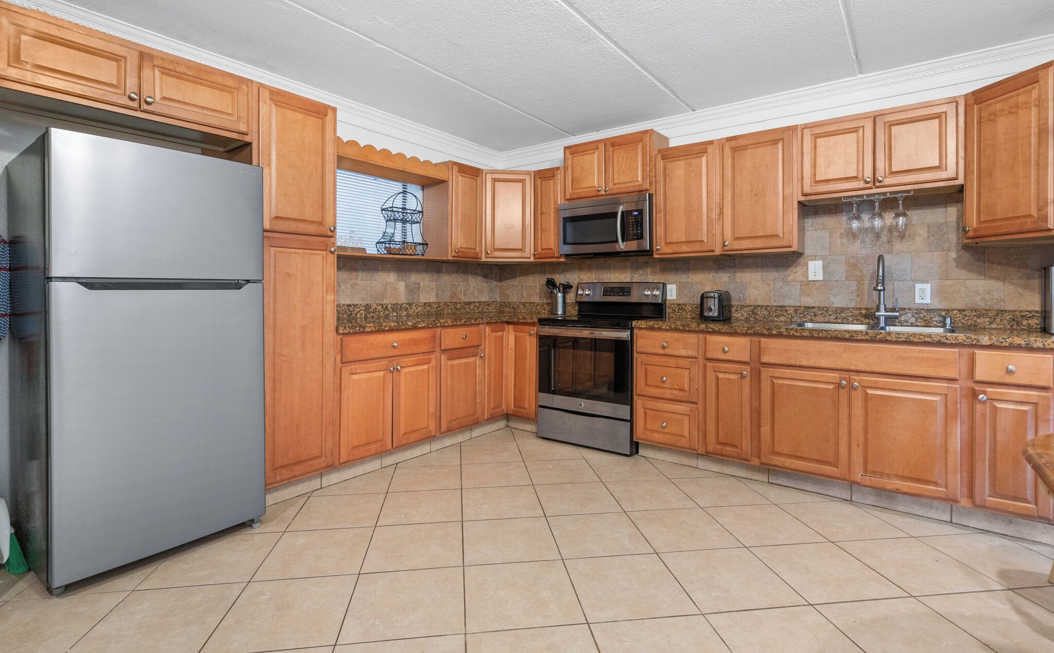 A kitchen with wooden cabinets, a stainless steel refrigerator, a microwave, an oven, and a granite countertop.