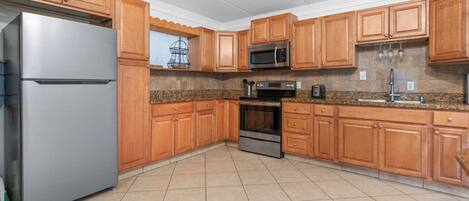 A kitchen with wooden cabinets, a stainless steel refrigerator, a microwave, an oven, and a granite countertop.