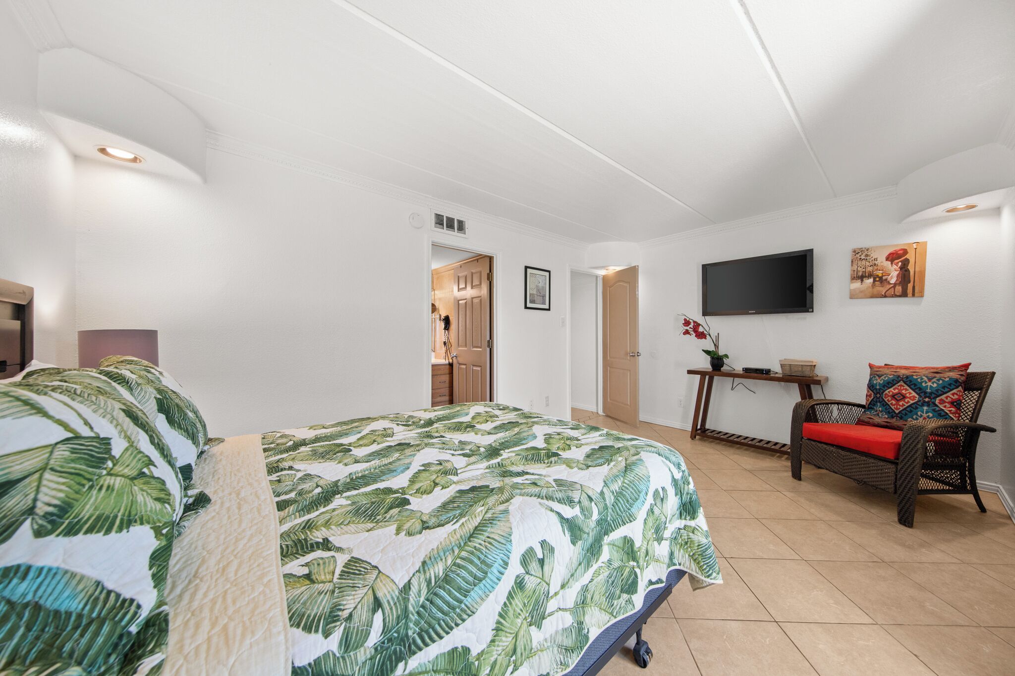 A bedroom with a bed, a TV, a chair, and a door leading to another room.