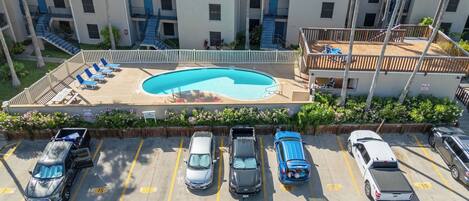 A multi-story building with a swimming pool, parking spaces, and a small garden area.