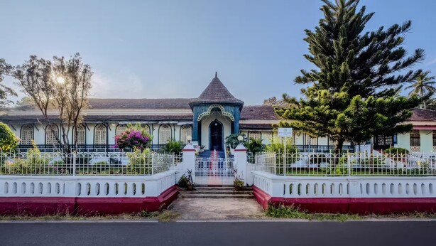 A traditional building with a central tower, surrounded by a white fence and a red and white painted wall. - La Maison by Dia Hotels and Homes (Panaji)
