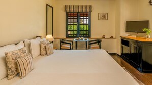 A hotel room with a large bed, a desk with chairs, a television, and a window with a view of greenery. - La Maison by Dia Hotels and Homes (Panaji)
